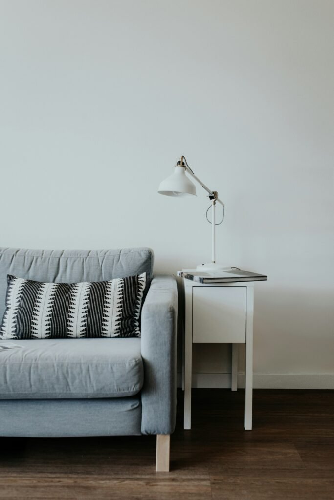 white study lamp on top of white wooden end table beside gray fabric sofa